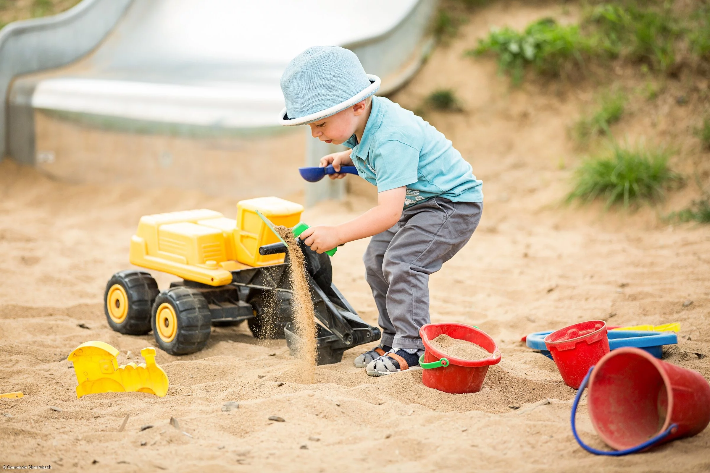 Ein Kind, umgeben von verschiedenen Spielsachen, spielt in einem Sandkasten