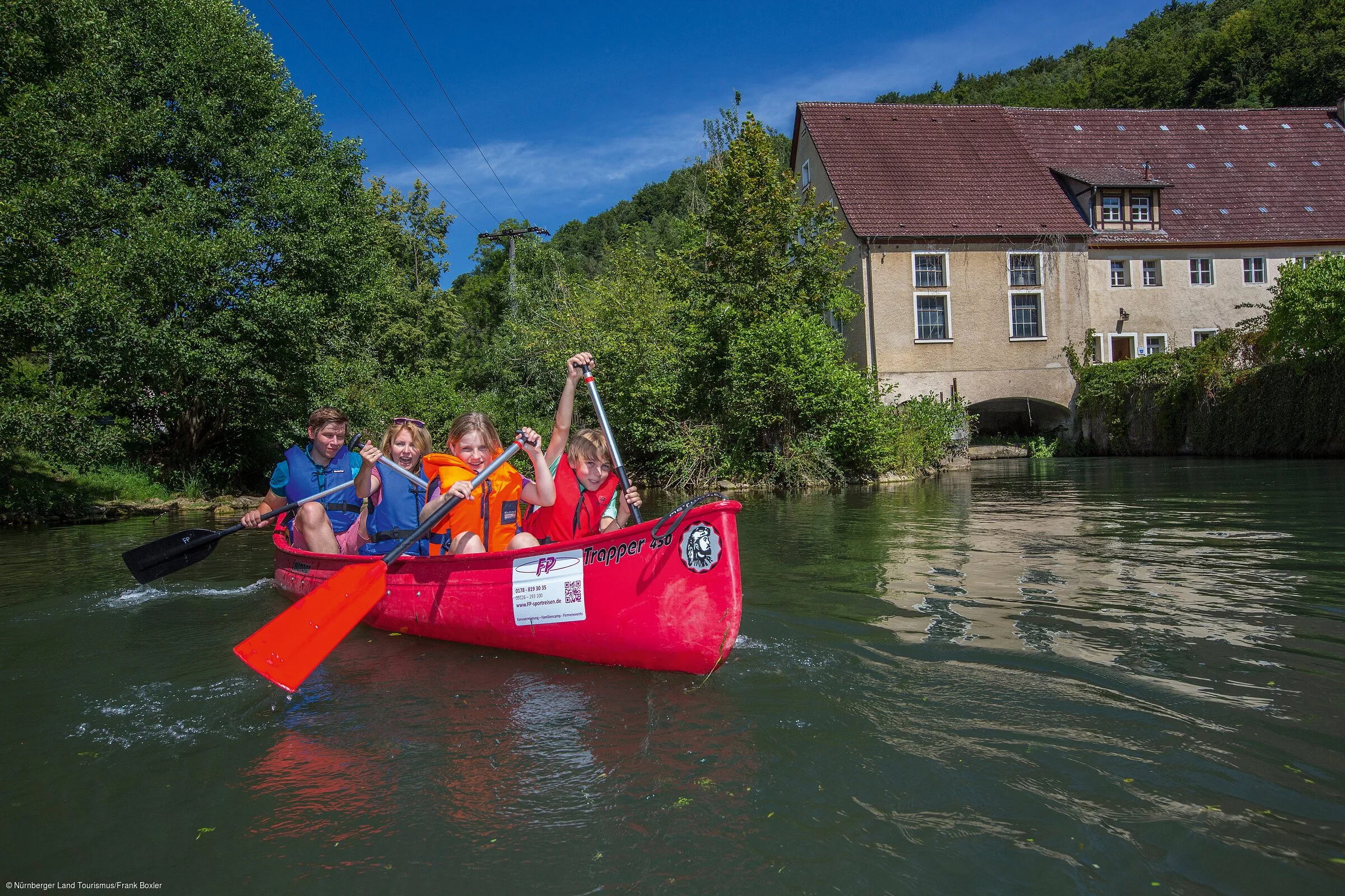 Eine Gruppe von Kindern in Schwimmwesten paddelt in einem roten Kanadier über eine Wasserfläche