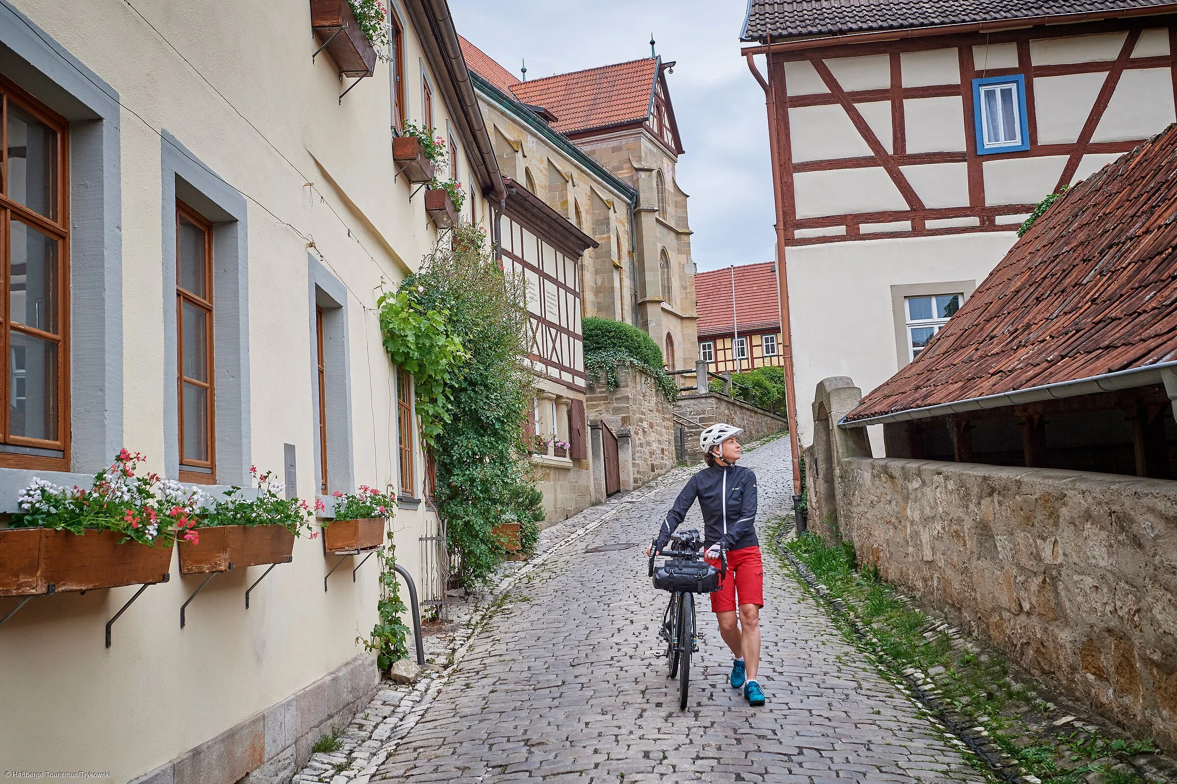 Eine Radlerin schiebt ihr Fahrrad durch historische Fachwerkkulisse