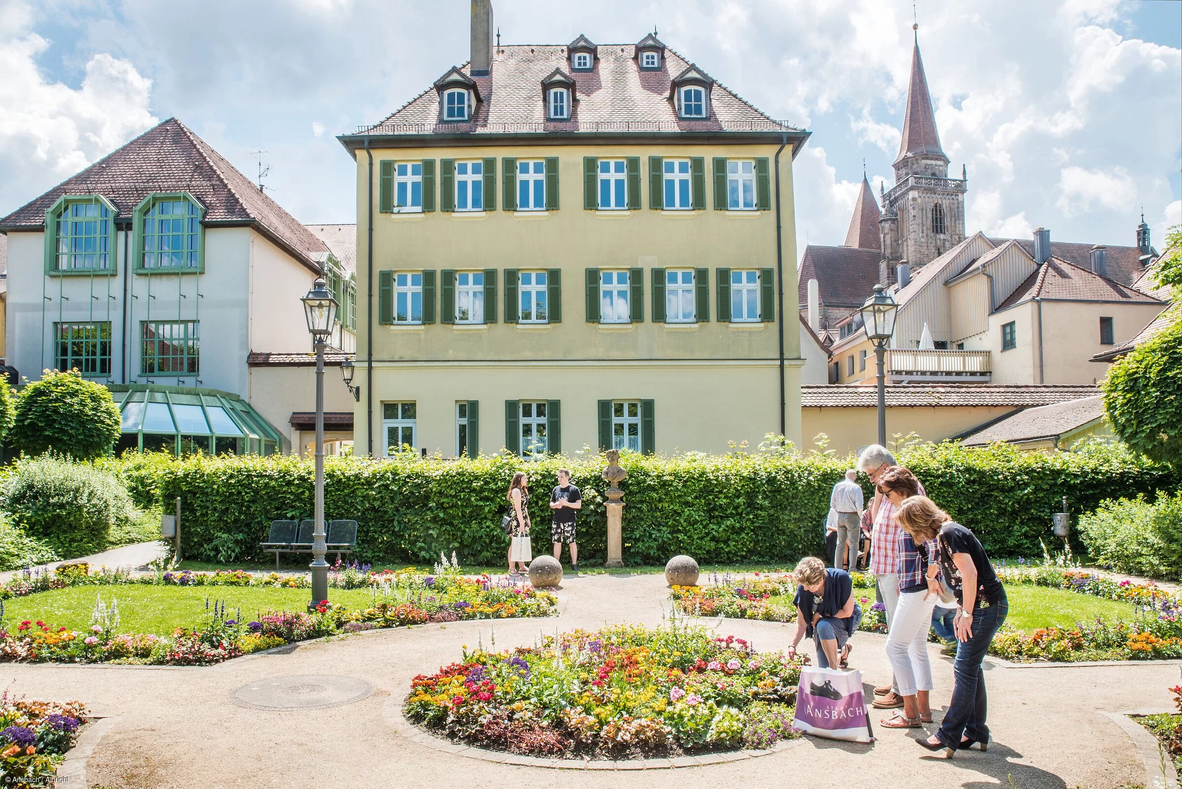 Eine Familie betrachtet beim Spazieren bunte Blumen in einem Park, dahinter eine Stadtkulisse