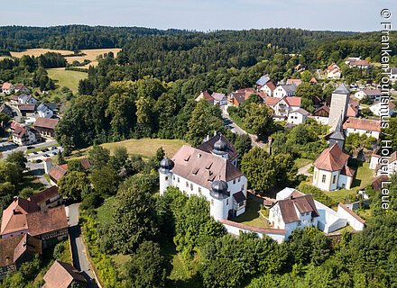 Ein sommerlicher Ort mit Schloss, umgeben von Wäldern und Feldern