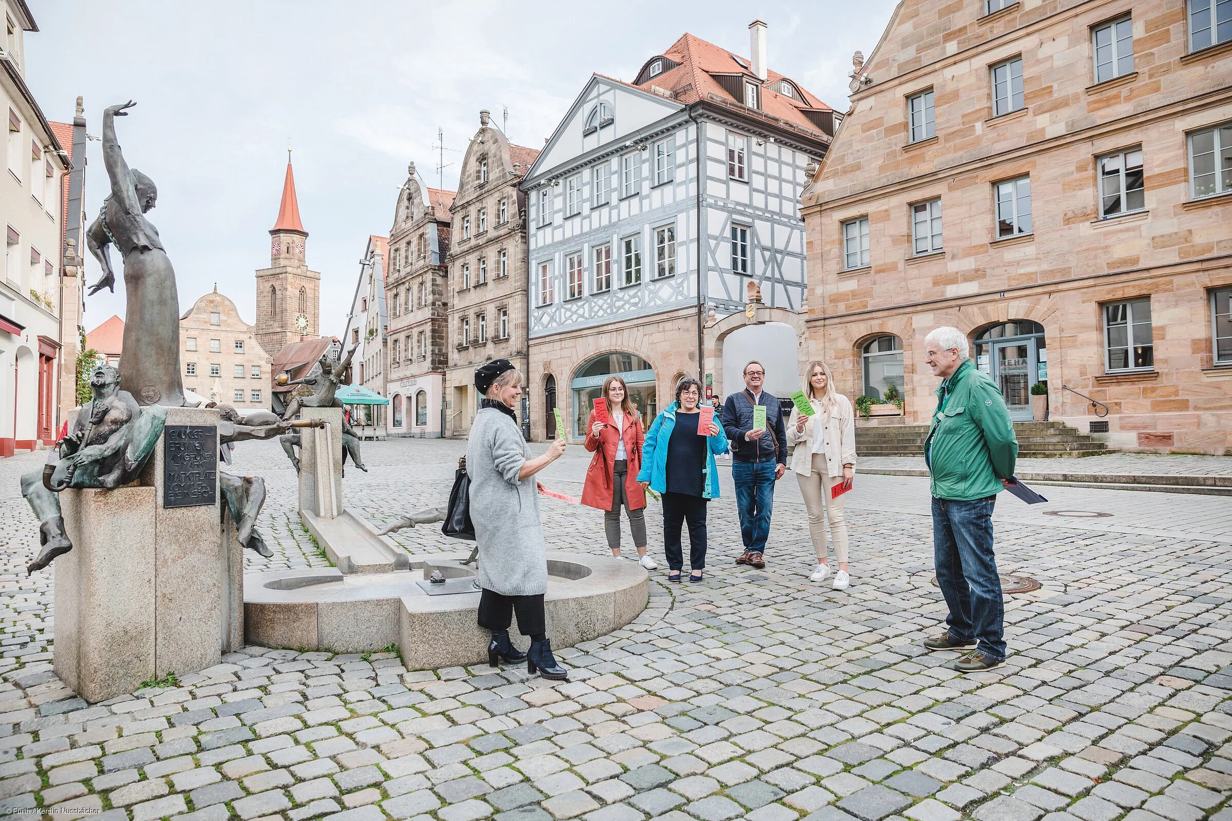 Ein Gruppe Leute während einer Stadtführung vor einem Brunnen, im Hintergrund Fachwerkhäuser