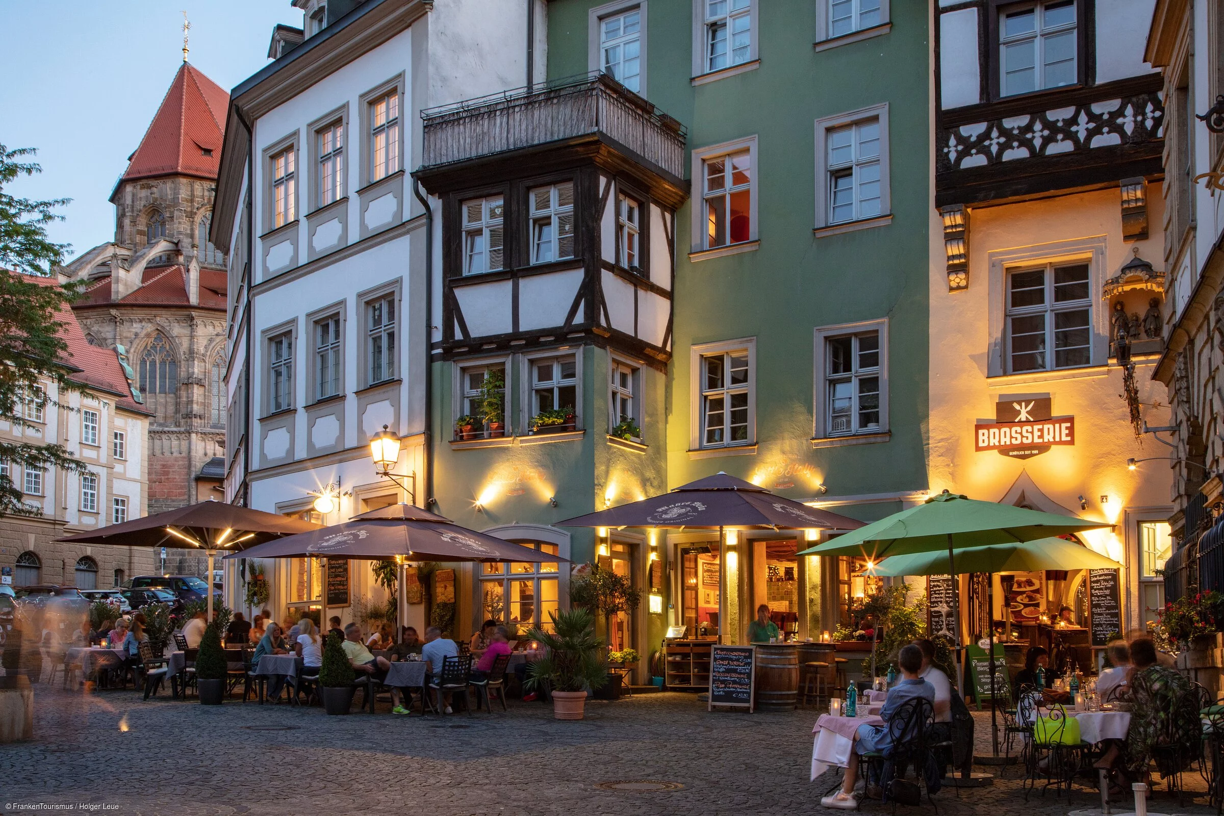 Eine abendliche Kulisse mit erleuchteten Biergärten in Fachwerkhäusern