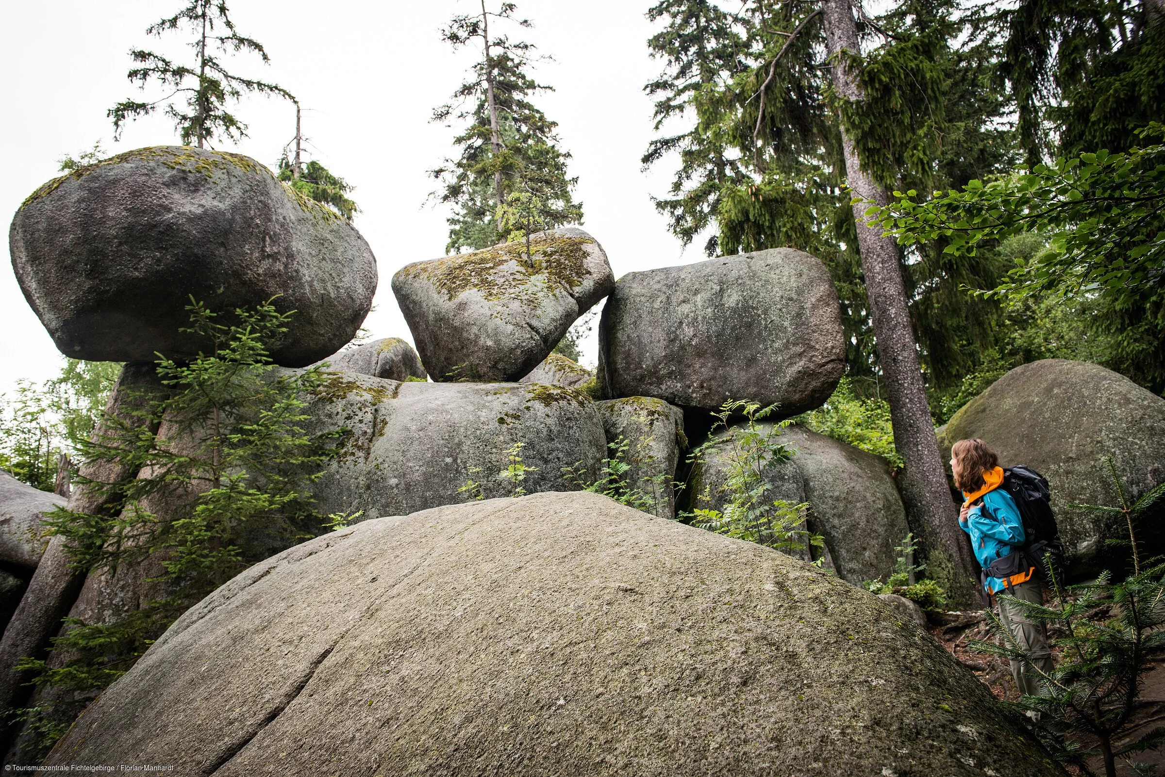 Eine mächtige Formation aus großen runden Felsen inmitten eines Waldes, davor eine Wanderin