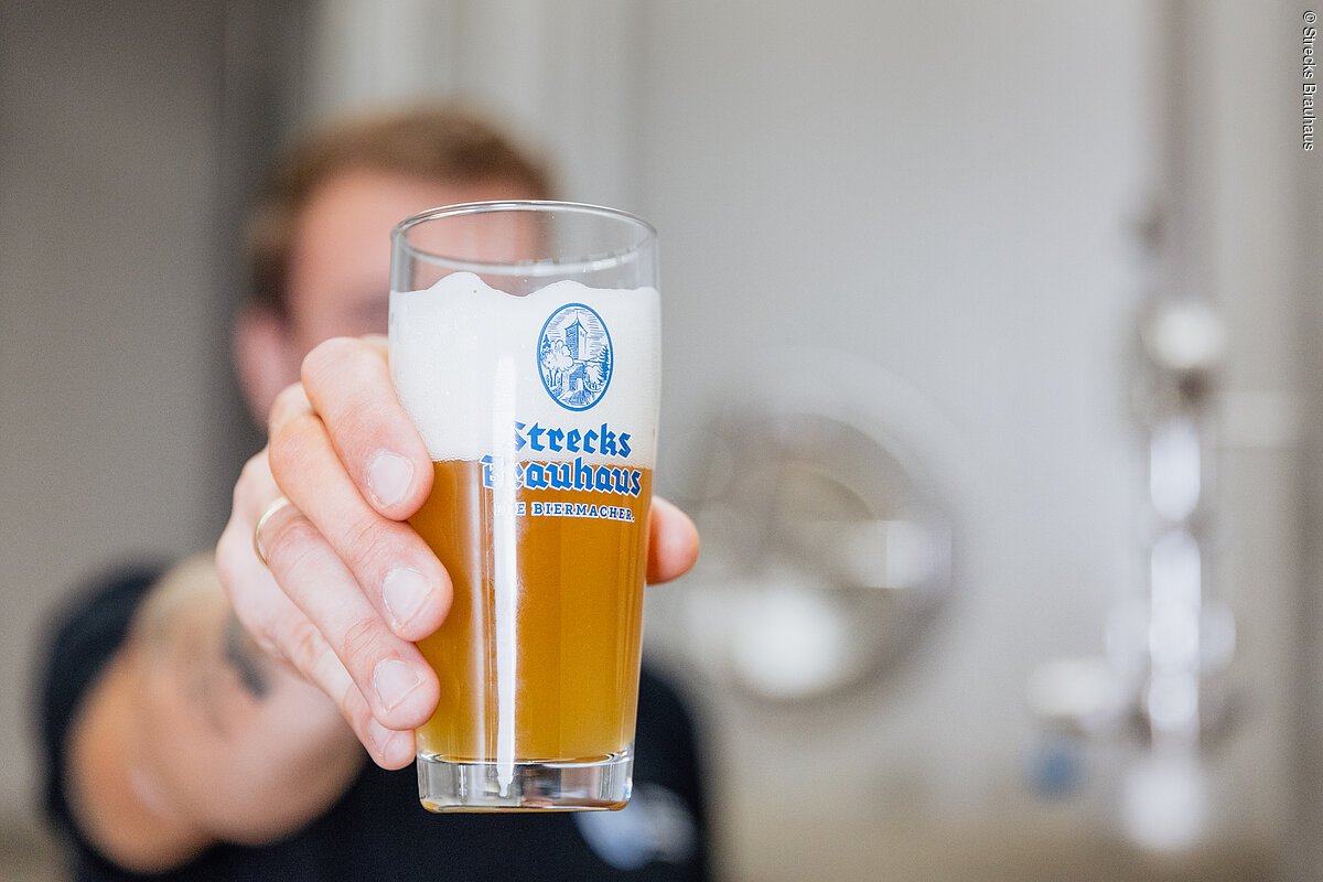 Strecks Brauhaus (Ostheim, Rhön) Eine Person hält ein Glas Bier mit Schaumkrone, darauf steht "Strecks Brauhaus".