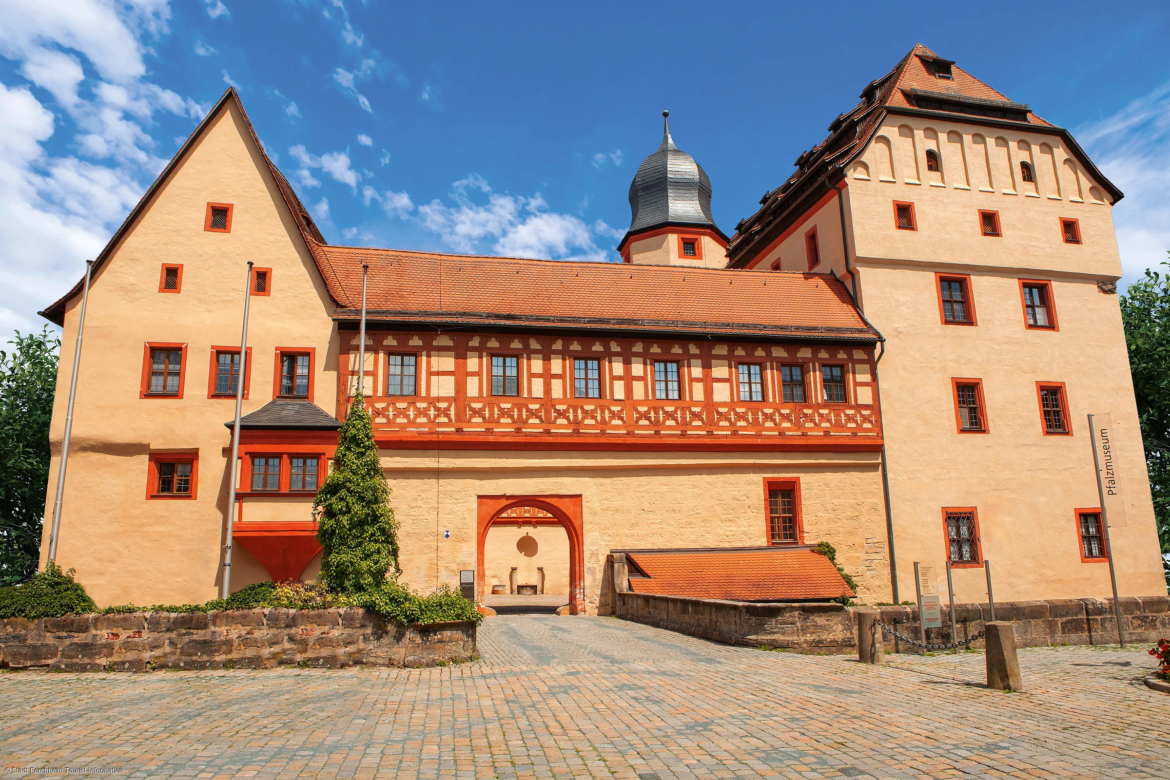 Historisches Gebäude mit Fachwerk und rotem Dach bei blauem Himmel, Pflastersteinweg im Vordergrund.